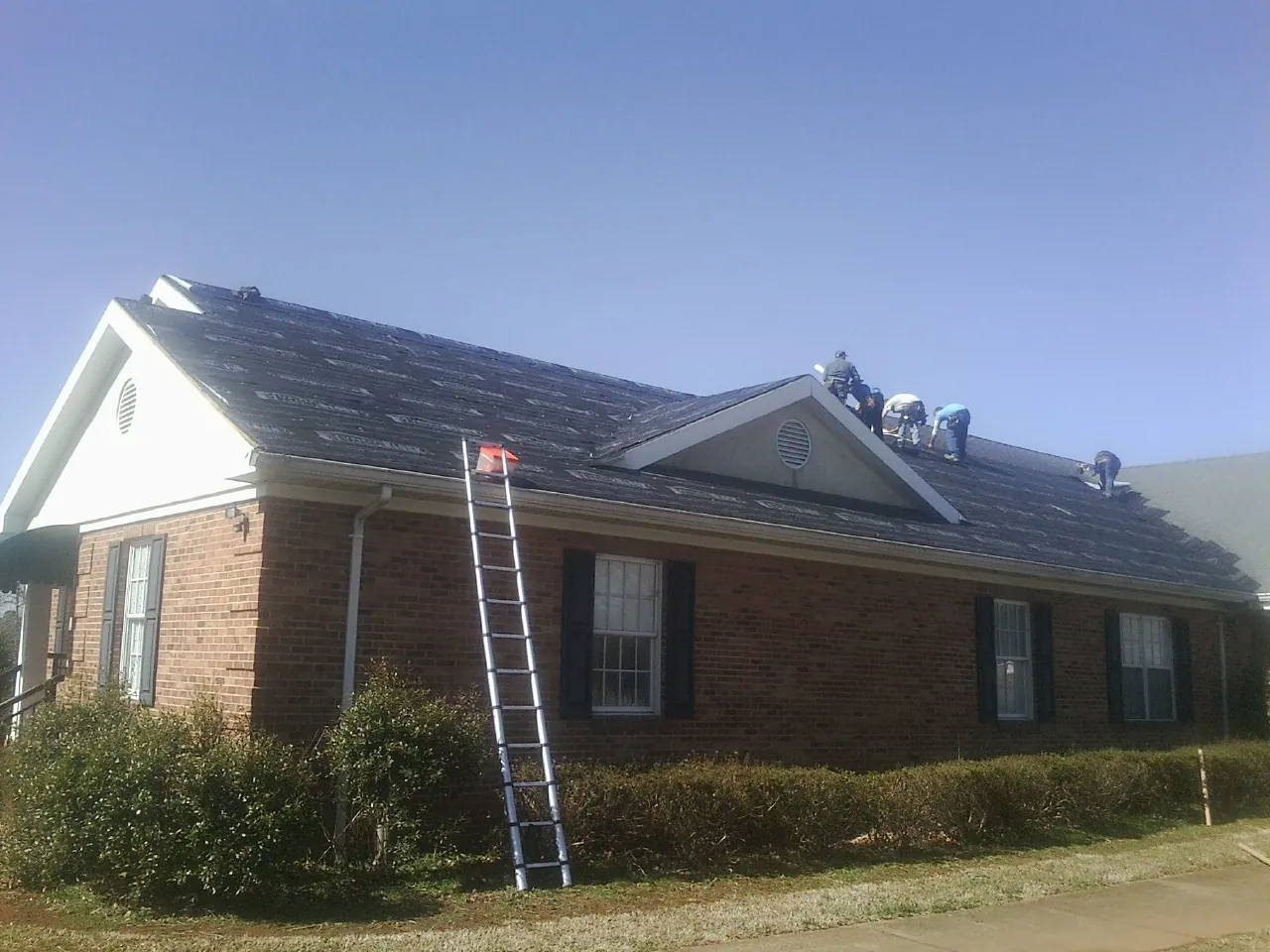 Crew tearing shingles off a brick ranch roof with a ladder set — Metal Roof Repair work by our crew in Moore