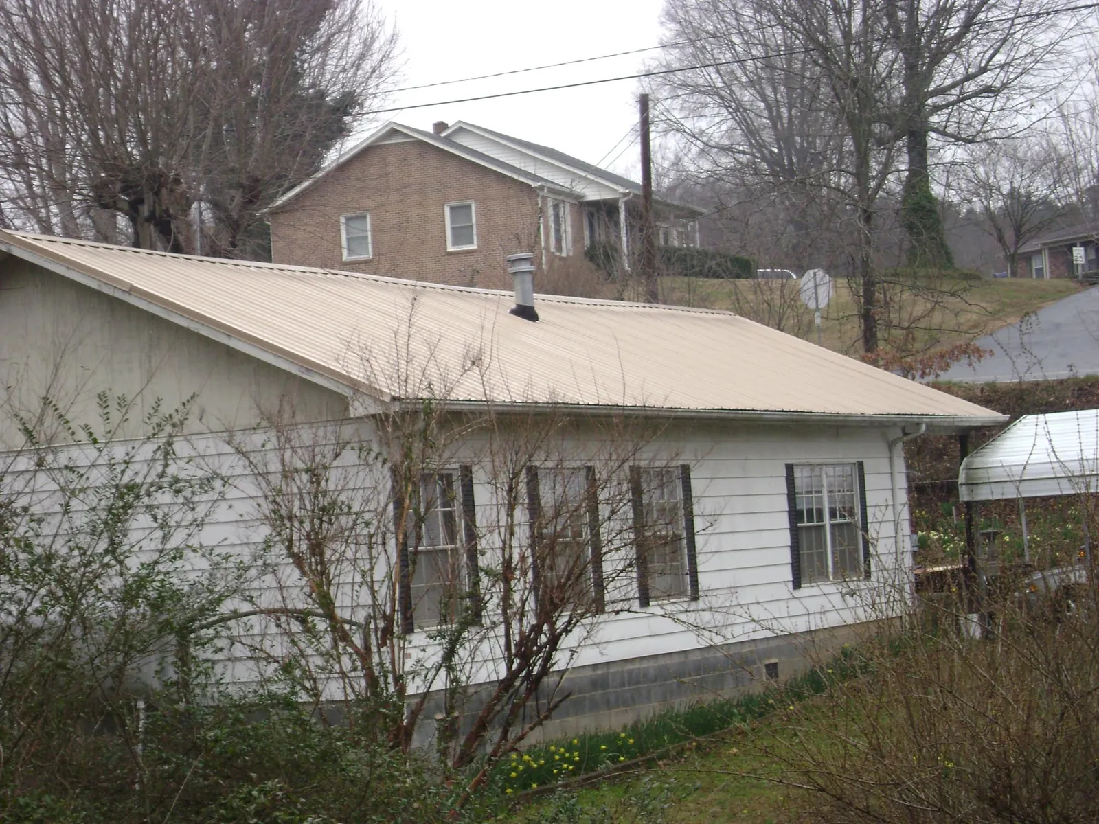 Tan metal roof on a white sided house set into a hillside — Commercial Roofing by Roofing Brothers in Moore
